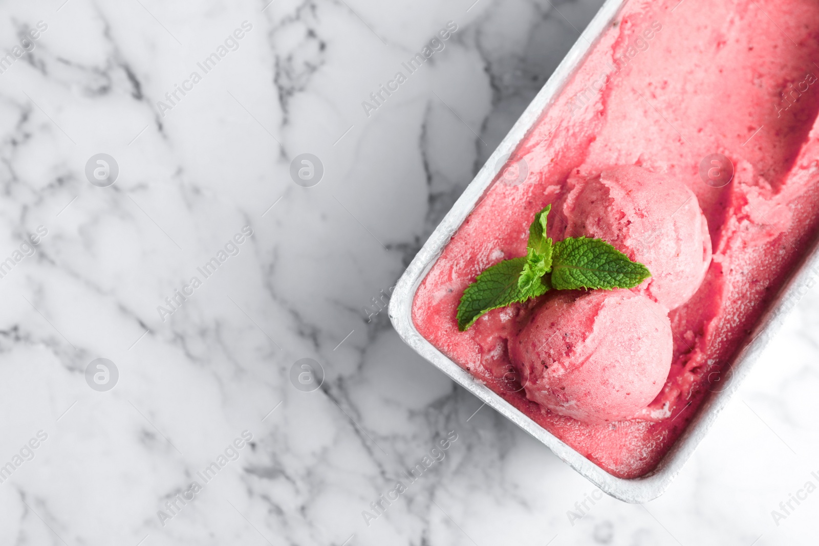 Photo of Container with delicious pink ice cream on marble table, top view. Space for text