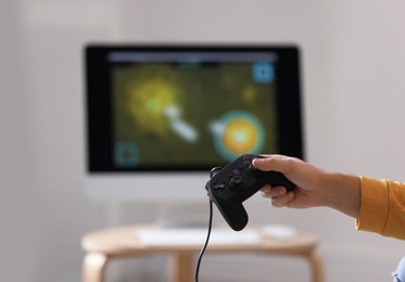 Photo of Young man holding video game controller against blurred background, closeup
