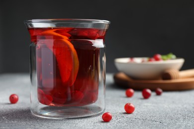 Photo of Tasty hot cranberry tea with lemon and fresh berries in glass on light grey textured table