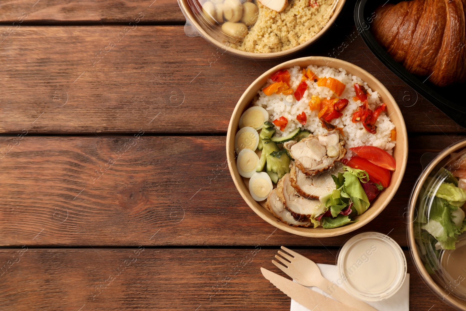 Photo of Tasty food in containers with knife and fork on wooden table, flat lay. Space for text