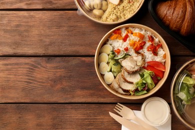 Tasty food in containers with knife and fork on wooden table, flat lay. Space for text