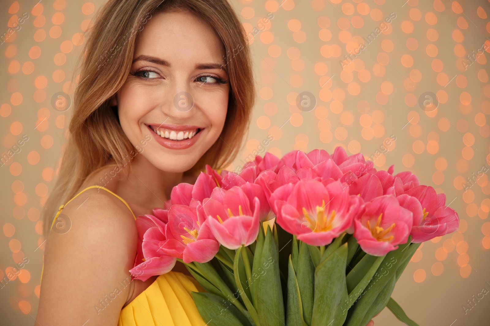 Photo of Portrait of smiling young girl with beautiful tulips on blurred background. International Women's Day