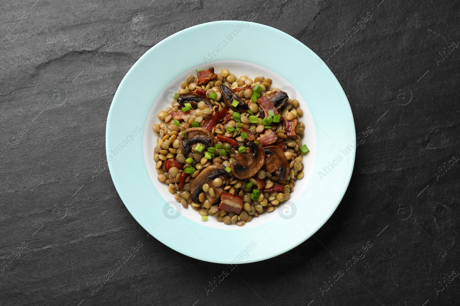 Photo of Delicious lentils with mushrooms, bacon and green onion on grey textured table, top view