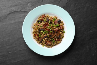 Photo of Delicious lentils with mushrooms, bacon and green onion on grey textured table, top view