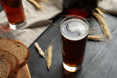 Photo of Glass of delicious kvass, bread and spikes on black table