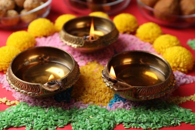 Diwali celebration. Diya lamps and colorful rangoli on red table, closeup