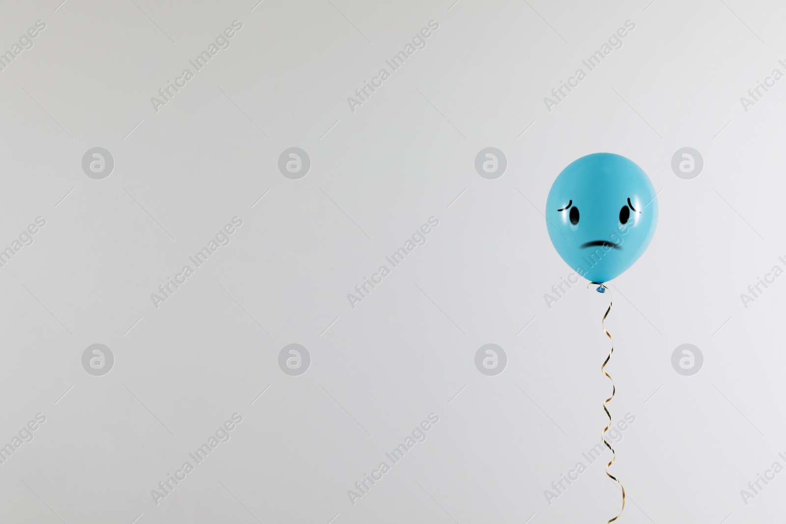 Image of Light blue balloon with sad face on grey background. Space for text