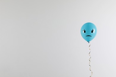 Light blue balloon with sad face on grey background. Space for text