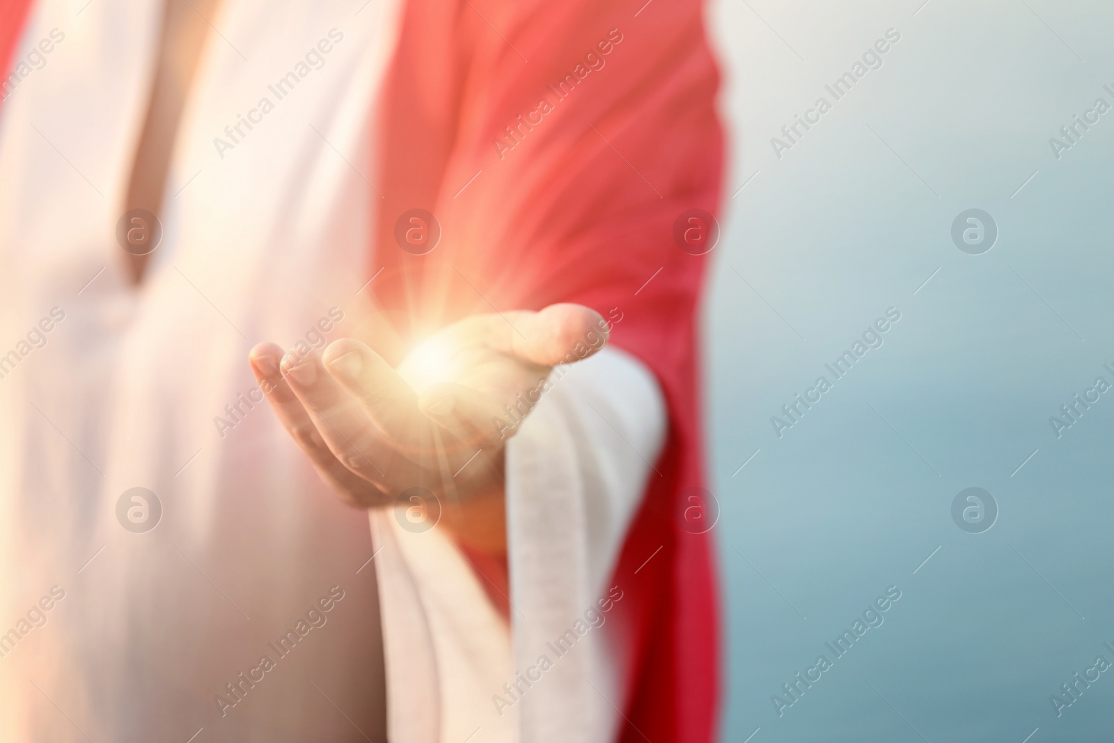 Image of Jesus Christ near water outdoors, closeup. Miraculous light in hand