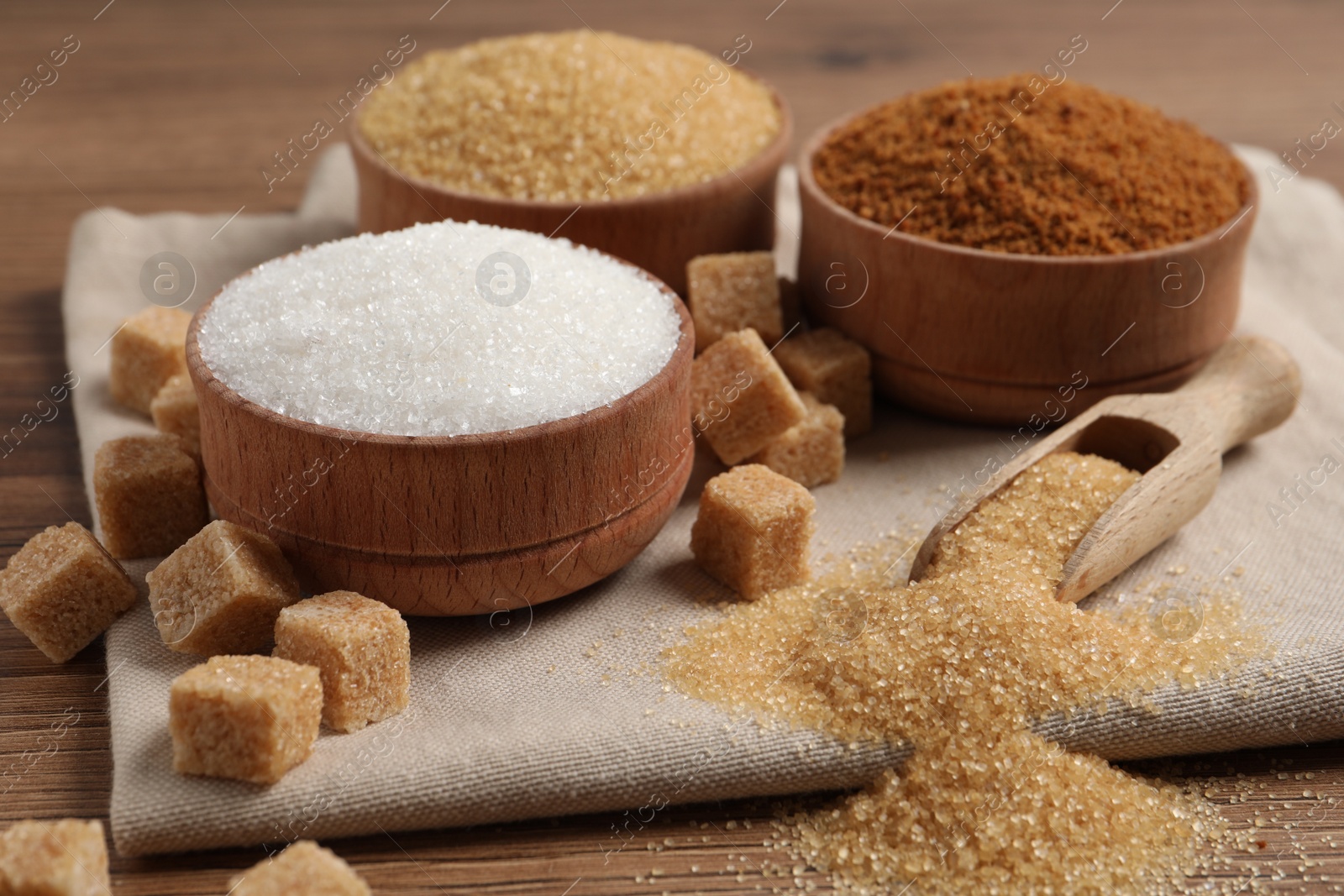 Photo of Different types of sugar in granules and cubes on wooden table, closeup