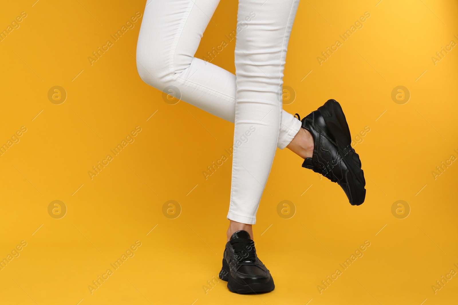 Photo of Woman wearing stylish sneakers on yellow background, closeup