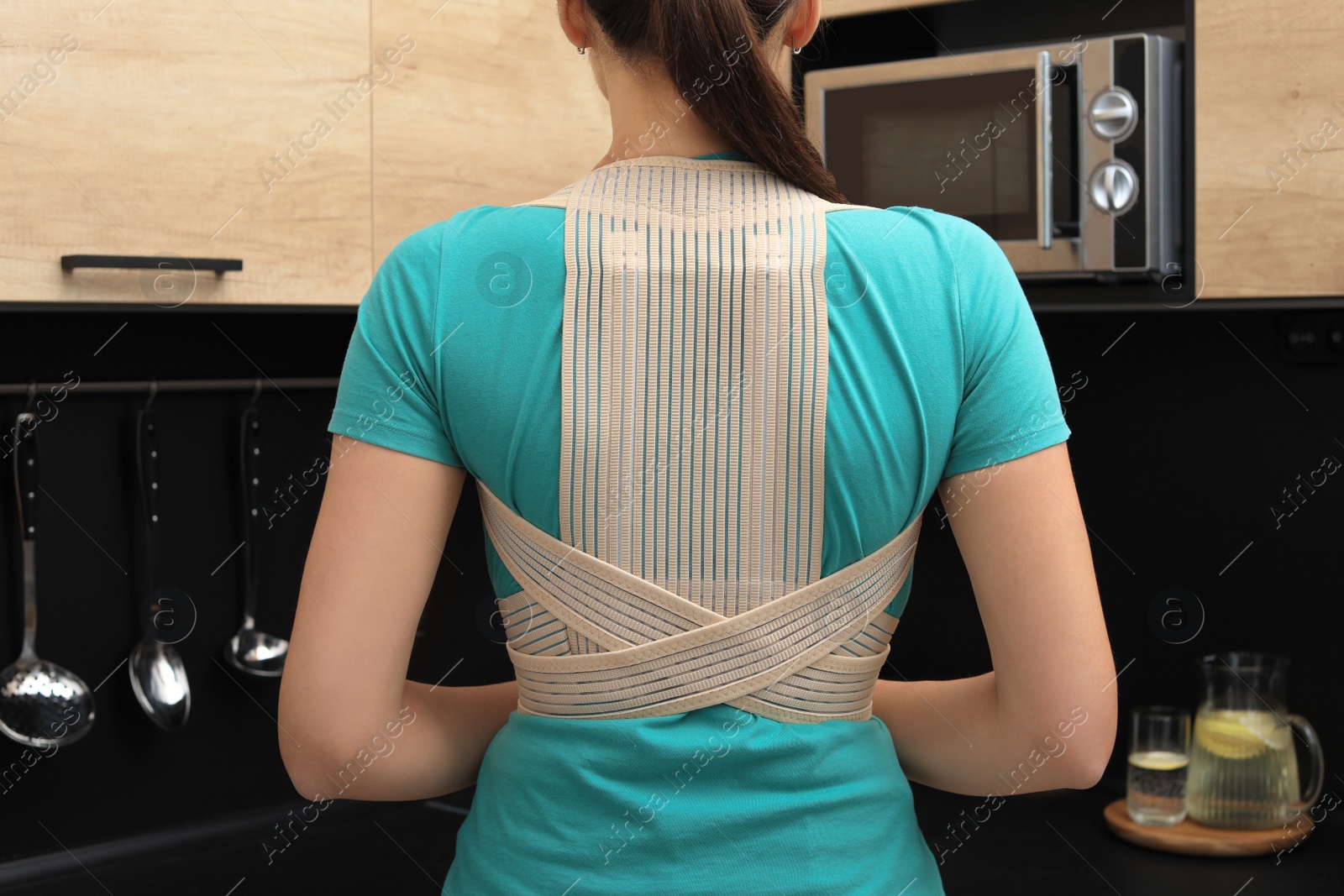 Photo of Woman with orthopedic corset in kitchen, back view