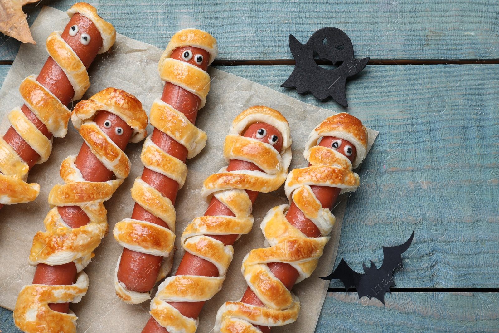 Photo of Cute sausage mummies served on blue wooden table, flat lay. Halloween party food