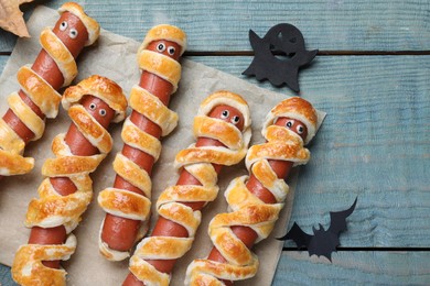 Cute sausage mummies served on blue wooden table, flat lay. Halloween party food