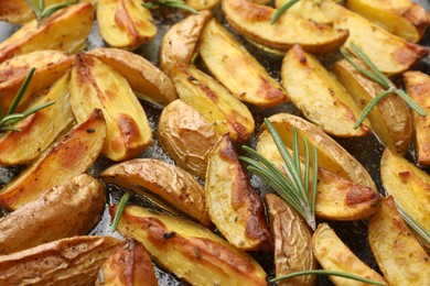 Photo of Delicious baked potatoes with rosemary on black surface, closeup