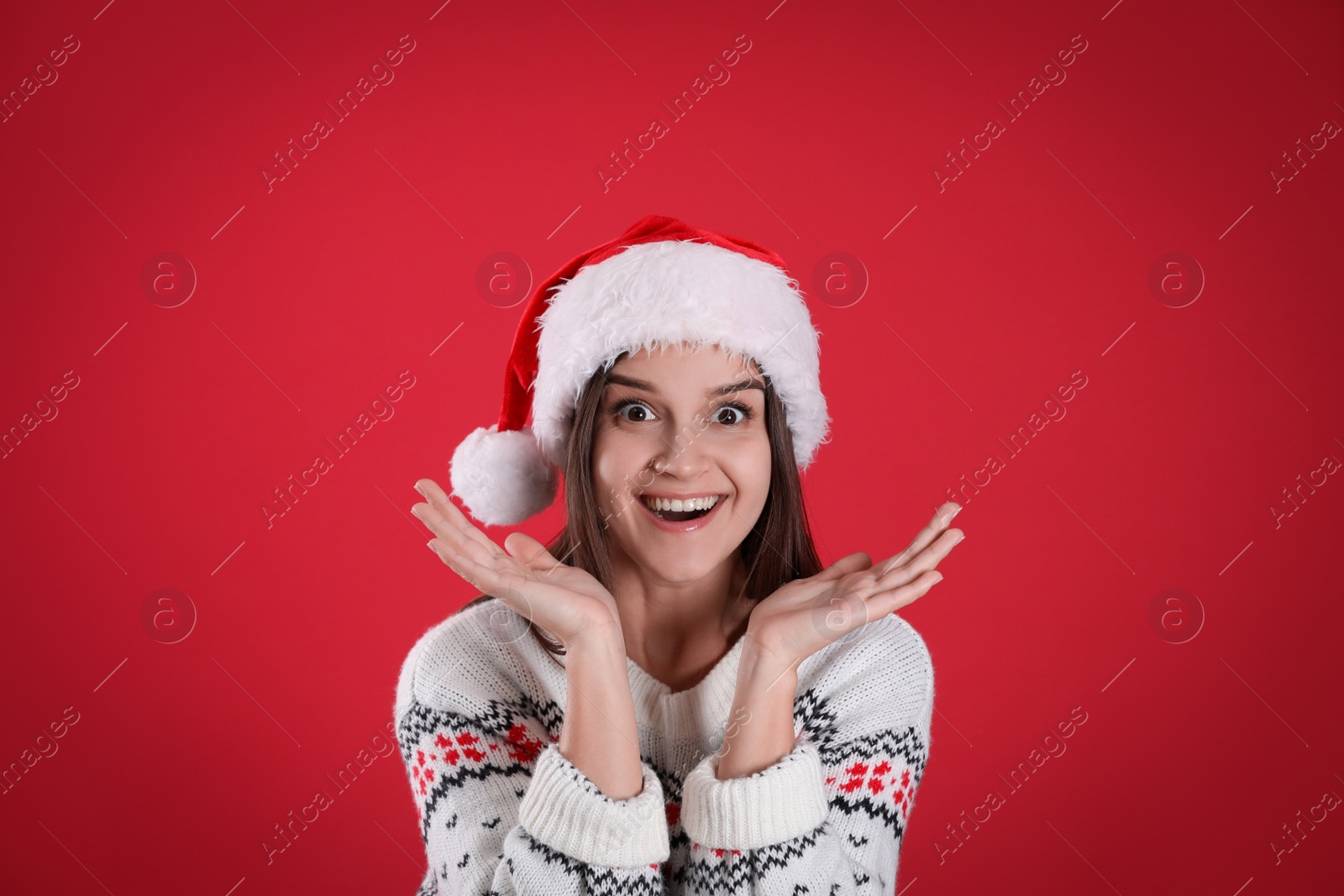 Photo of Surprised woman in Santa hat and Christmas sweater on red background