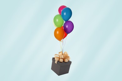 Many balloons tied to gift box on light blue background