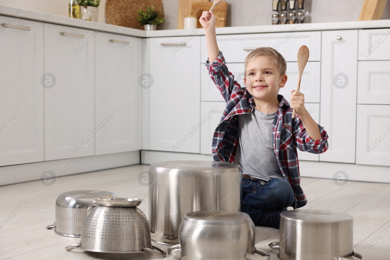 Photo of Little boy pretending to play drums on pots in kitchen