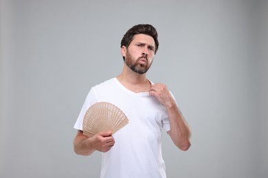 Photo of Unhappy man with hand fan suffering from heat on light grey background