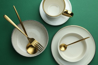 Stylish empty dishware and golden cutlery on green background, flat lay