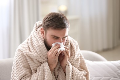 Photo of Young man suffering from runny nose in living room