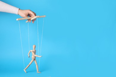 Woman pulling strings of puppet on light blue background, closeup