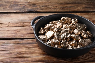 Photo of Pan of gold nuggets on wooden table. Space for text