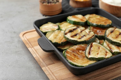 Photo of Grill pan with delicious zucchini slices on grey table. Space for text