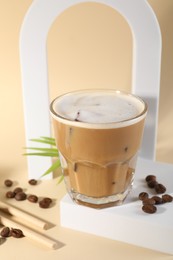 Refreshing iced coffee with milk in glass and beans on pale yellow background