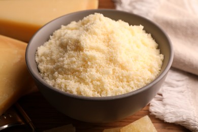 Photo of Delicious grated parmesan cheese in bowl on wooden table, closeup
