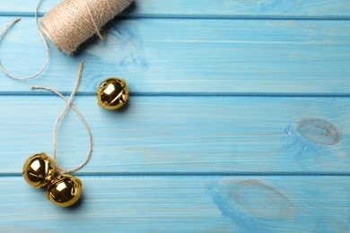 Golden sleigh bells and rope on light blue wooden background, flat lay. Space for text