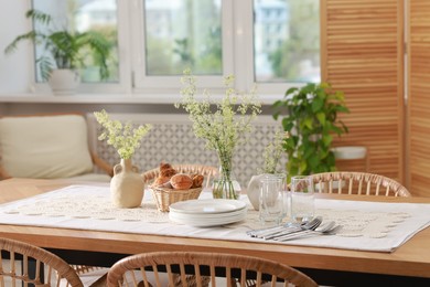 Photo of Clean dishes, flowers and fresh pastries on table in stylish dining room