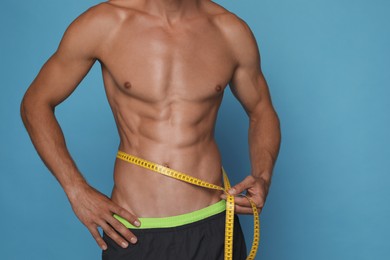 Photo of Shirtless man with slim body and measuring tape around his waist on light blue background, closeup