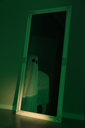 Photo of Creepy ghost. Woman covered with sheet in green light, reflection in mirror