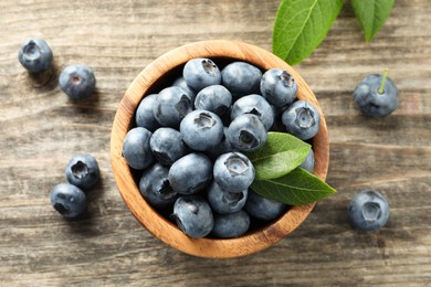 Photo of Bowl of fresh tasty blueberries on wooden table, flat lay