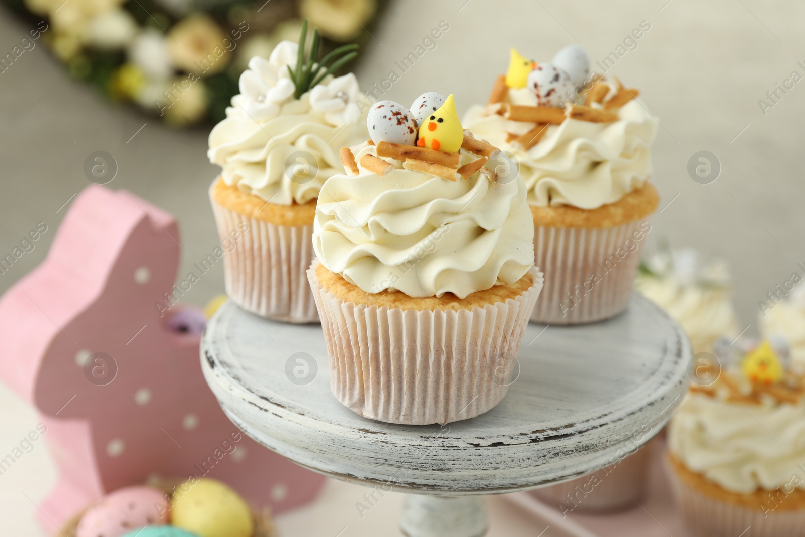 Photo of Tasty Easter cupcakes with vanilla cream and festive decor on cake stand, closeup