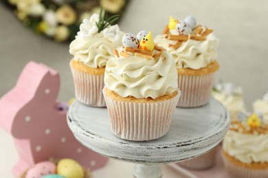 Tasty Easter cupcakes with vanilla cream and festive decor on cake stand, closeup