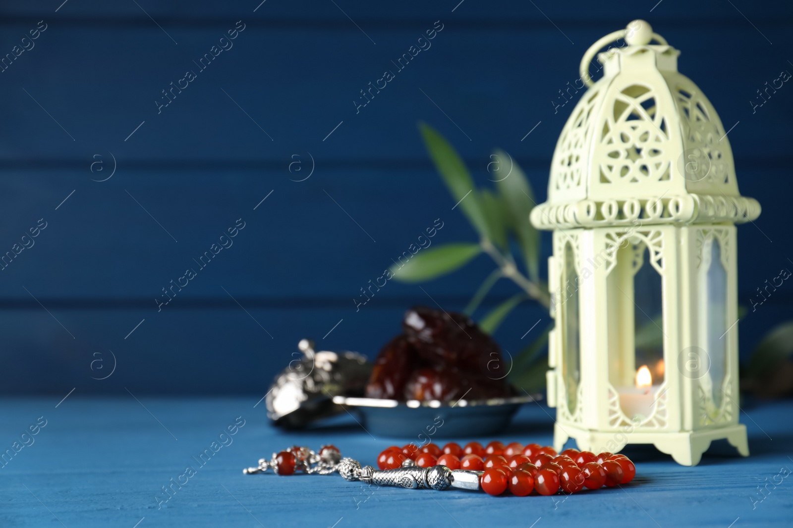 Photo of Arabic lantern and misbaha on light blue wooden table. Space for text