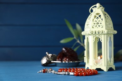 Photo of Arabic lantern and misbaha on light blue wooden table. Space for text