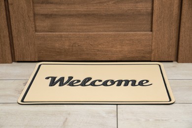 Photo of Beautiful beige doormat with word Welcome on floor near entrance