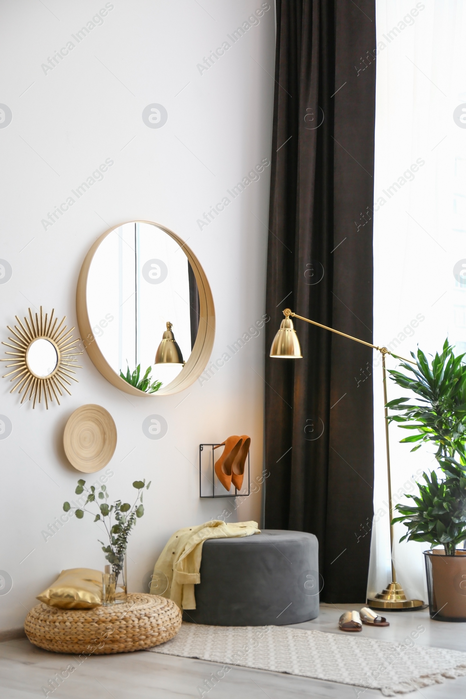 Photo of Hallway interior with big round mirror and ottoman chair near white wall