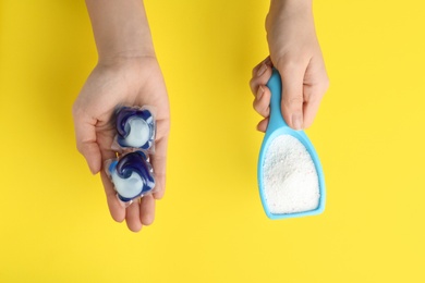 Woman holding laundry capsules and detergent powder on yellow background, top view