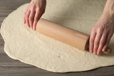 Photo of Woman rolling raw dough at wooden table, closeup