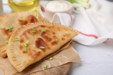 Photo of Delicious fried chebureki with cheese and green onion on white textured table, space for text