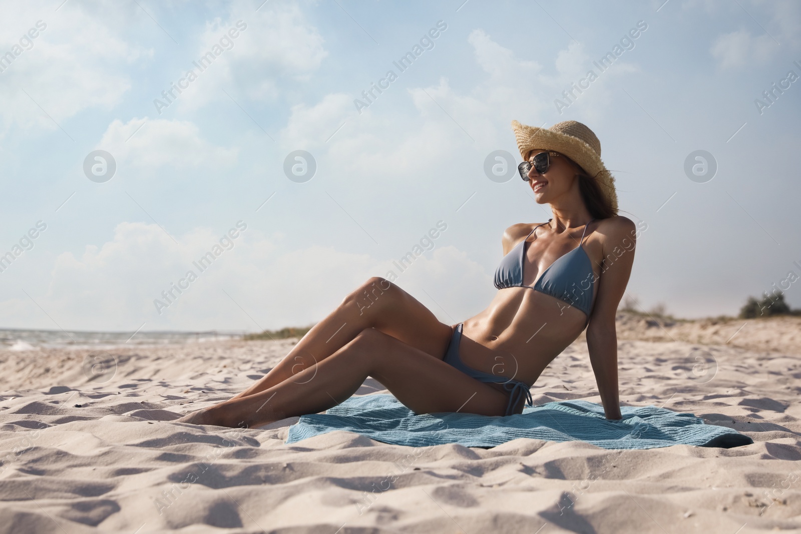 Photo of Attractive woman with straw hat sitting on beach towel near sea