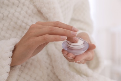 Photo of Woman holding jar with cream on light background, closeup