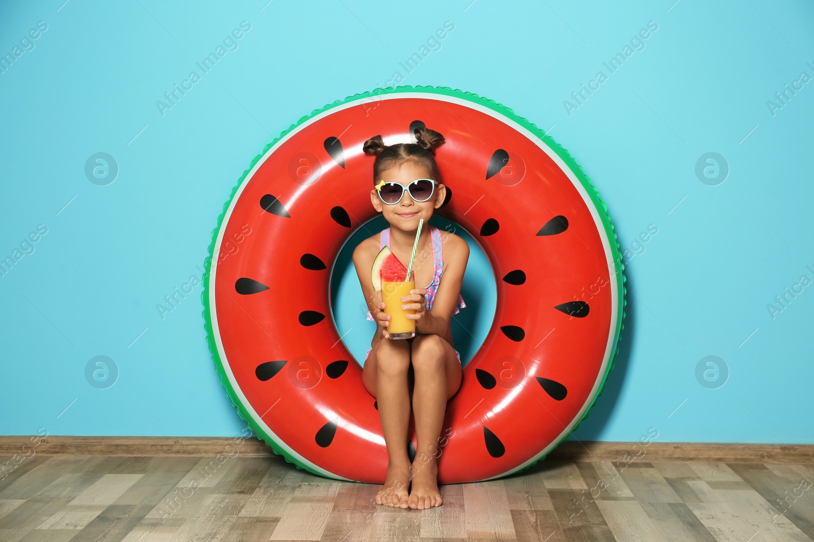 Photo of Cute little girl with inflatable ring and glass of cocktail near color wall