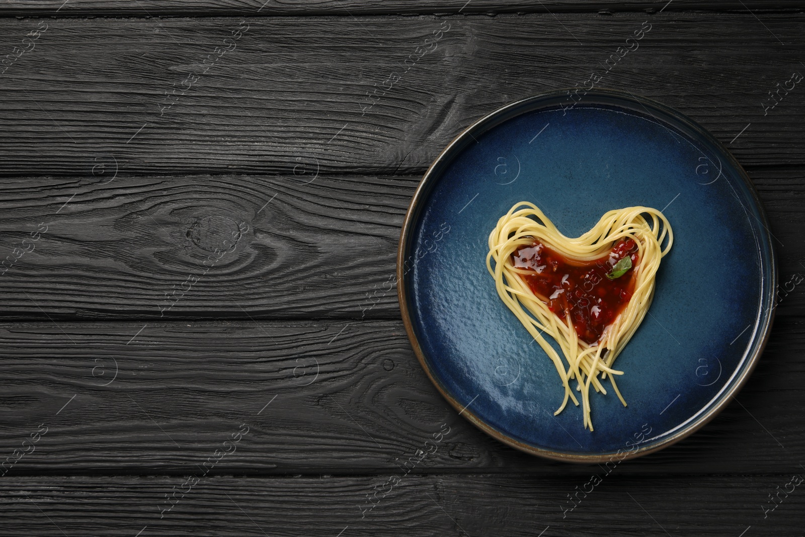 Photo of Heart made with spaghetti and sauce on black wooden table, top view. Space for text