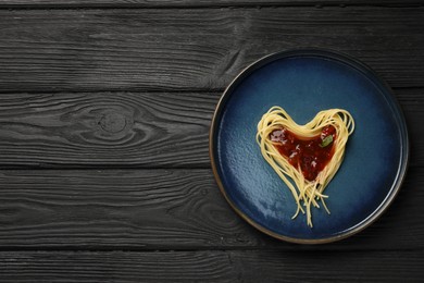 Heart made with spaghetti and sauce on black wooden table, top view. Space for text