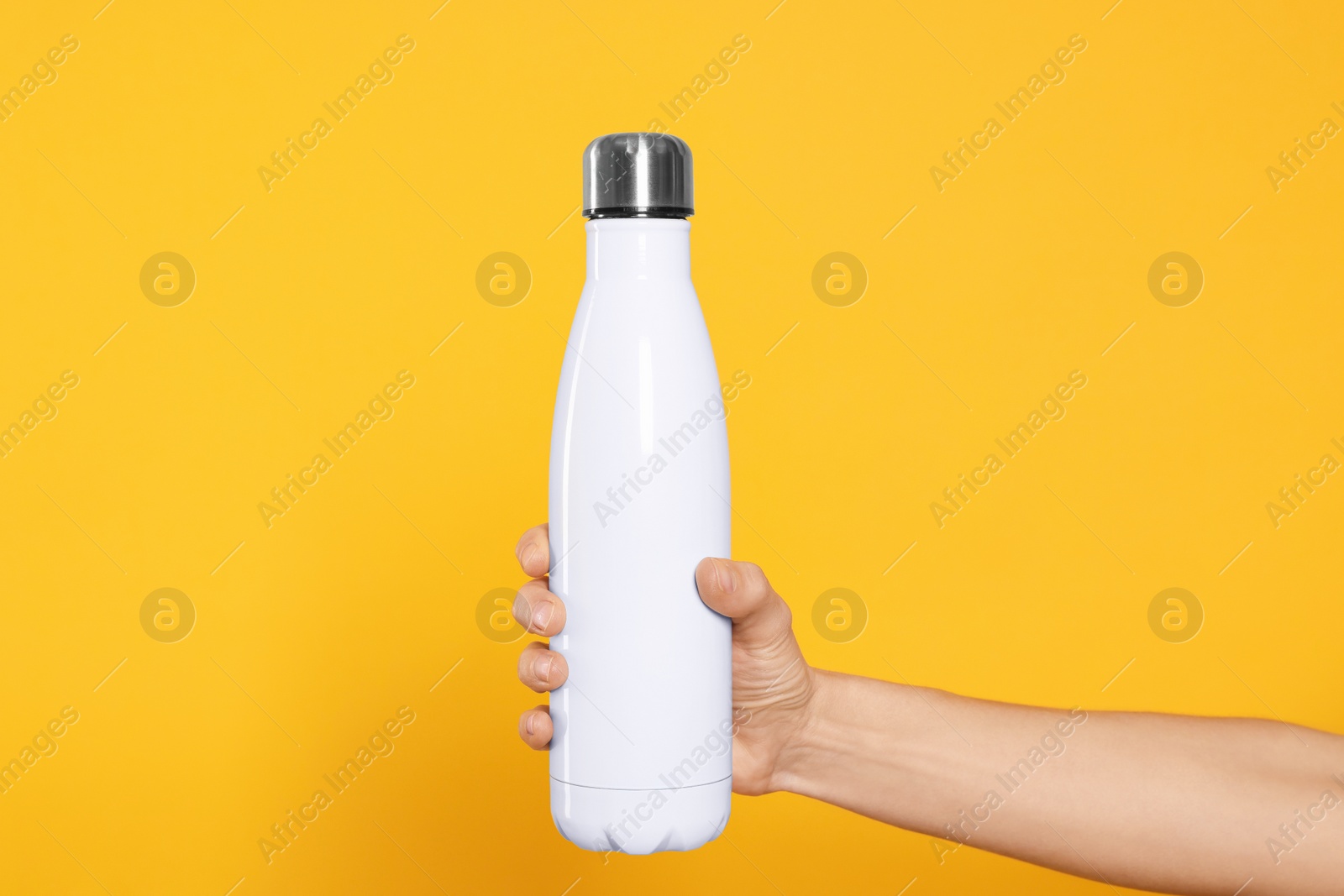 Photo of Woman holding thermo bottle of drink on orange background, closeup